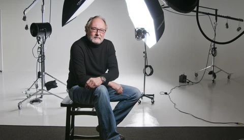 Man sitting on stool in professional studio with softbox lighting setup.