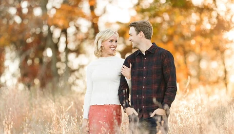 Couple walking together in an autumn field with warm, golden-hour backlighting.