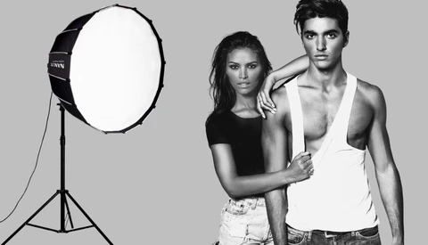 Two models pose together in a studio with a large softbox light positioned to the left.
