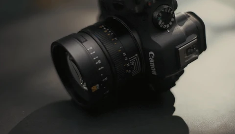 Canon DSLR camera with attached telephoto lens on gray surface with soft lighting.