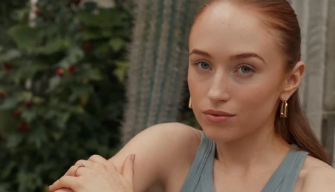 Woman with reddish-brown hair wearing a gray tank top, looking directly at camera with a neutral expression.