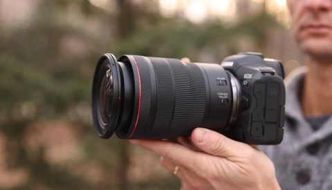 Photographer holding a Canon RF-mount mirrorless camera with a telephoto zoom lens attached.