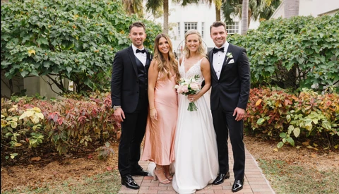 Bride and groom pose with two groomsmen in a garden courtyard surrounded by ivy and flowering shrubs.