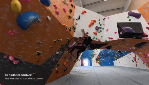 Indoor rock climbing wall with colorful holds viewed from below, showing multiple climbing routes and angles.