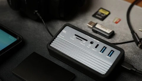Multi-port USB hub with card reader and cables on dark desk surface.