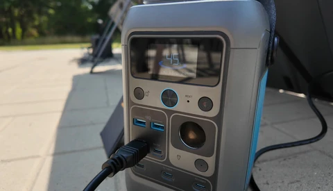 Portable power station with display screen, control buttons, and USB ports, photographed outdoors on pavement.