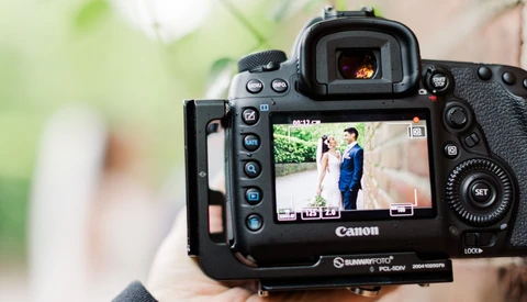 Canon DSLR camera displaying wedding photography on its rear LCD screen, held at an event with blurred background.