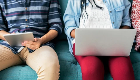 Three people sitting on a teal couch, each holding a laptop or tablet device.