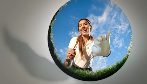 Woman in white shirt crouching in grass, framed within a circular vignette showing blue sky above.