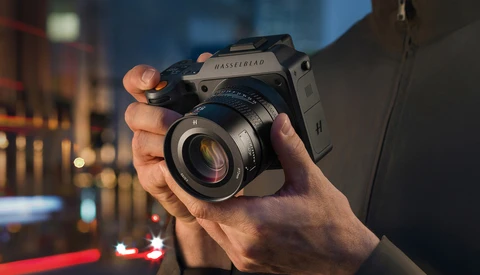 Photographer holding a medium format film camera with a prime lens against an urban nighttime backdrop.