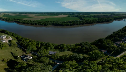 Aerial view of a meandering river with forested banks and farmland beyond.