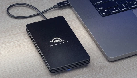 External hard drive connected via USB cable next to a laptop on a wooden desk.