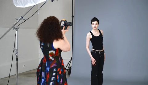Photographer shooting a portrait of a woman in a studio with professional lighting setup.