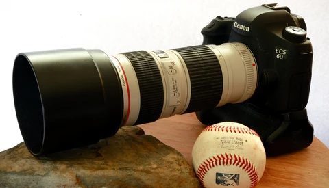 Canon EOS 6D DSLR camera with telephoto lens, baseball, and rock on wooden surface.