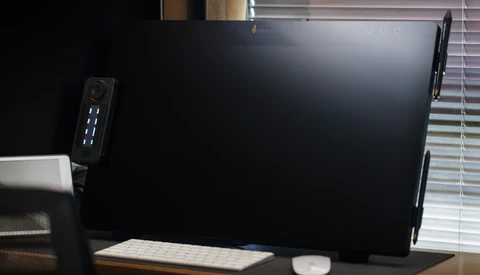 Desktop workspace with a large monitor, compact tower PC with illuminated ports, wireless keyboard, and mouse on a wooden desk.