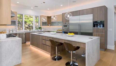 Modern kitchen with wood cabinetry, white quartz countertops, stainless steel appliances, and a large island with seating.
