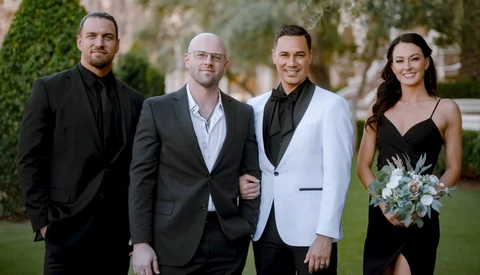 Four people in formal attire standing outdoors on a lawn with architectural backdrop.