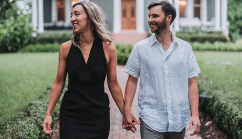 Couple walking hand-in-hand through a manicured garden in front of a residential home.