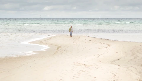 Lone figure standing on a curved sandbar extending into shallow turquoise water.