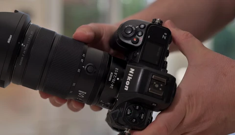 Hand holding a Nikon Z mirrorless camera with attached zoom lens in outdoor setting.
