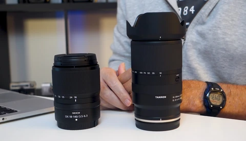 Two black camera lenses displayed side by side on a white surface, with a person's hand holding the larger telephoto lens.