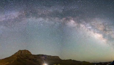 Milky Way galaxy stretches across night sky above a dark mountain silhouette.