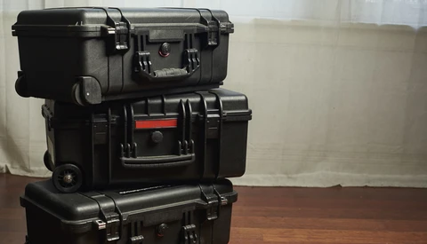 Three stacked black protective hard cases with handles and latches on a wooden surface.