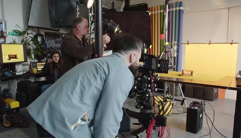 Filmmaker operating a cinema camera on a gimbal stabilizer in a studio with yellow backdrop and lighting equipment.