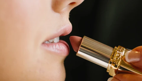 Close-up of lips with gold-toned lipstick applicator positioned near mouth.