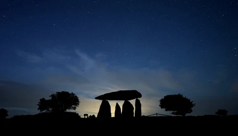 Silhouette of ancient stone monument against twilight sky with stars and surrounding trees.