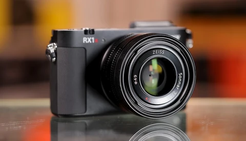 Sony RX1 compact camera with Zeiss lens on reflective surface against warm-toned background.