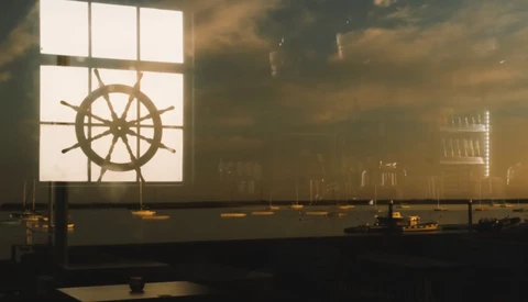 Ship's wheel silhouetted against a bright window in warm, atmospheric interior lighting.