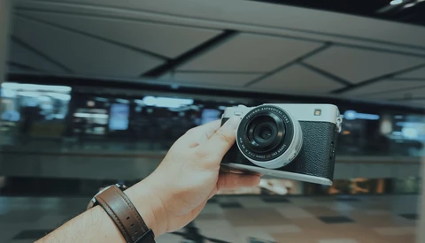 Person holding a vintage rangefinder camera with leather strap in an indoor terminal or station setting.