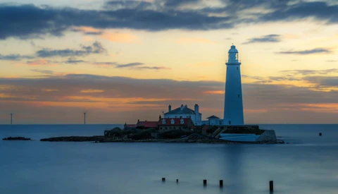 Lighthouse on rocky island at twilight with long exposure water effect.