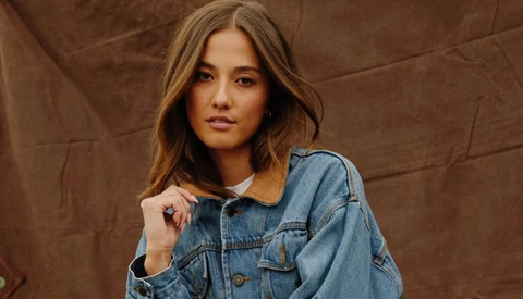 Woman wearing a denim shirt with corduroy collar against a brown fabric backdrop.