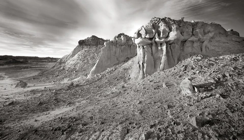 Dramatic rock formations and eroded cliffs in an arid landscape under stormy skies.