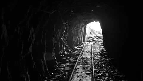 Railroad tracks disappearing into a dark tunnel with bright light visible at the far end.