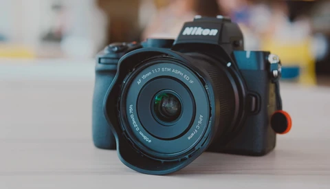 Nikon mirrorless camera with blue body and standard zoom lens on neutral surface.