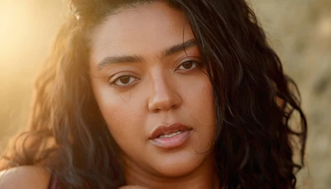 Portrait of a woman with long dark wavy hair, looking directly at camera with warm golden hour lighting.