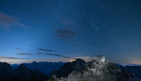 Hilltop castle silhouetted against starry night sky with mountain range in twilight.