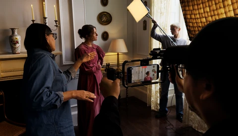 Behind-the-scenes film production in an elegant interior with crew operating camera and lighting equipment.