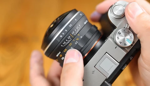 Hands holding a vintage rangefinder camera with an interchangeable lens mounted on top.