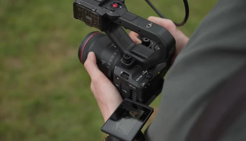 Videographer holding a professional cinema camera with external monitor mounted on top.