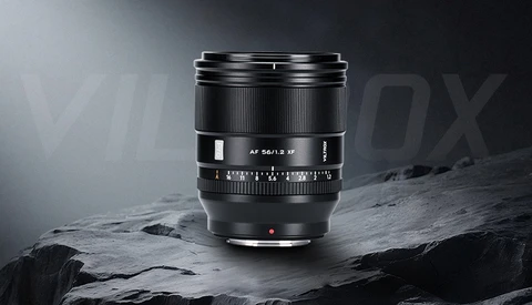 Black camera lens with manual focus ring and depth-of-field scale mounted on rocky surface.