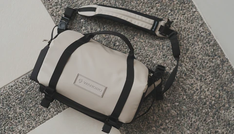 White and black compact camera bag with shoulder strap on gray textured fabric.