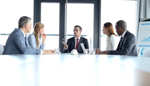 Five business professionals seated at a conference table during a meeting.
