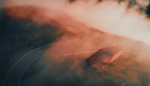 Red canoe on still water surrounded by misty forest landscape with warm, hazy light filtering through fog.