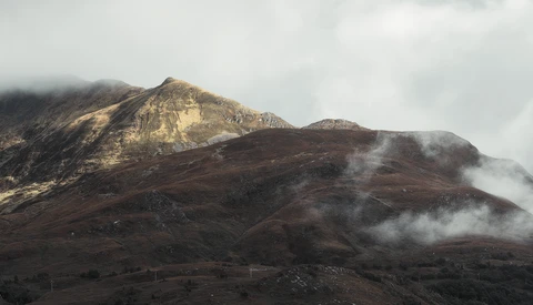 Volcanic mountain with golden-lit peak and dark slopes partially shrouded in white steam and clouds.