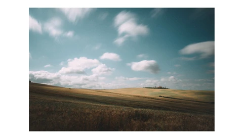 Rolling agricultural landscape with plowed and golden fields under a partly cloudy sky.