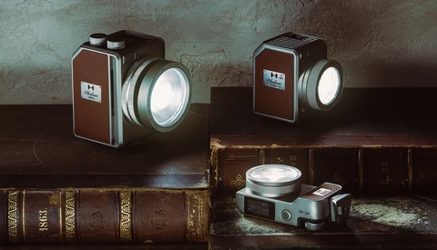 Three vintage film cameras with illuminated lenses arranged on antique leather-bound books against a textured wall.